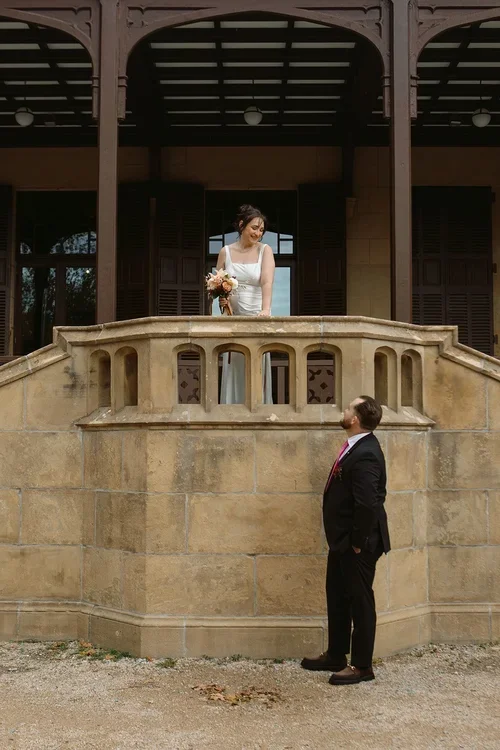 Bride on a stone castle balcony smiling down at groom below at a wedding venue in Malaga