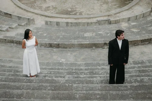 Bride in white midi dress and groom in black suit standing apart on the ancient Roman amphitheatre steps in Malaga