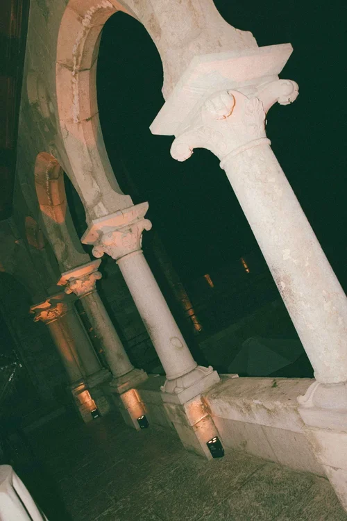 Ancient carved stone arches and columns with ornate capital details illuminated by warm amber uplighting at a historic Malaga wedding venue at night