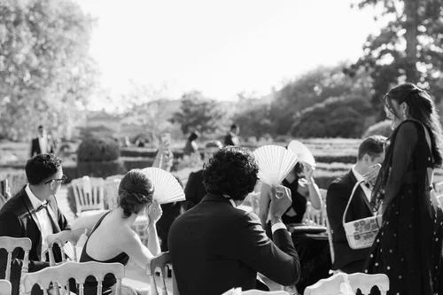 Wedding guests fanning themselves with white paper fans during a sunny outdoor wedding ceremony in Marbella