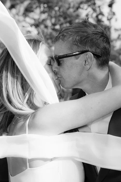 A bride and groom kissing surrounded by the brides silk scarf flowing in the wind