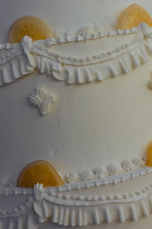 Close-up macro detail of tall white wedding cake tiers with piped ruffle swag decoration and amber sugar gem embellishments