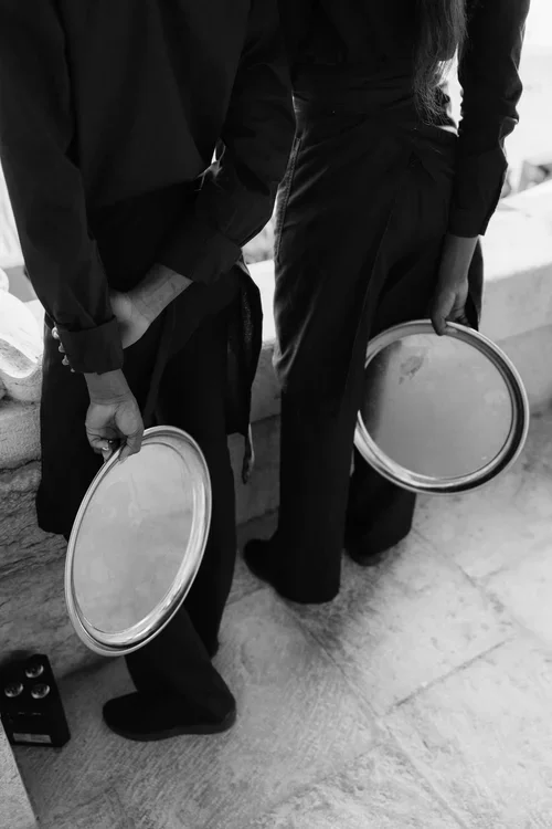 Close crop of two waiters in black uniforms holding empty silver oval serving trays at a wedding reception on a marble floor