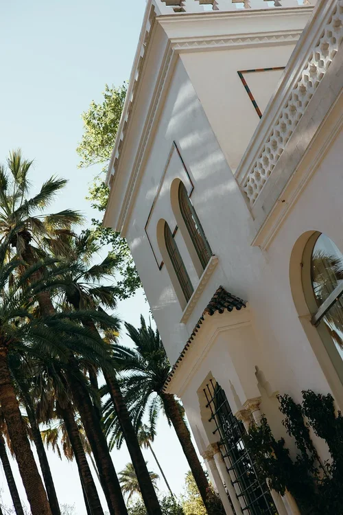Upward angle of a grand white Moorish-style wedding venue building surrounded by palm trees in Seville