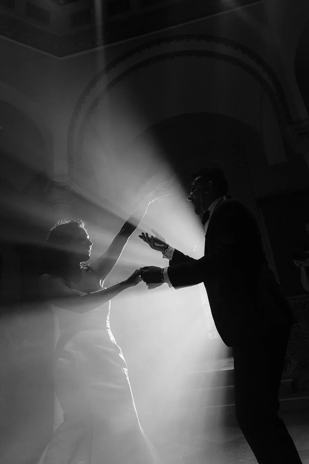 Bride and groom first dance silhouette lit by dramatic light beams in a grand ballroom