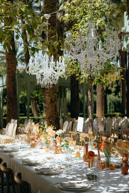 Marbella luxury wedding with a long outdoor table setting and hanging chandeliers surrounded by palm trees