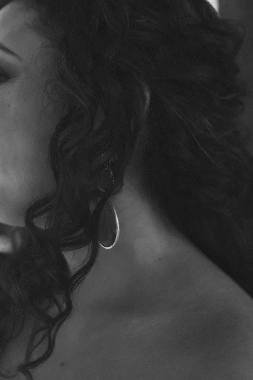 Moody black and white close-up of bride with dark curly hair and gold hoop earring