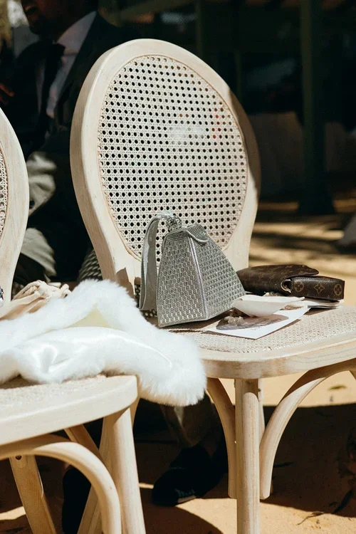 Wedding ceremony rattan chairs with a designer handbag, Louis Vuitton wallet and white feather wrap on the seat