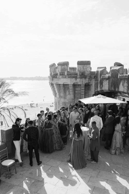 Wedding guests mingling on a medieval stone castle terrace overlooking a beach and coastline