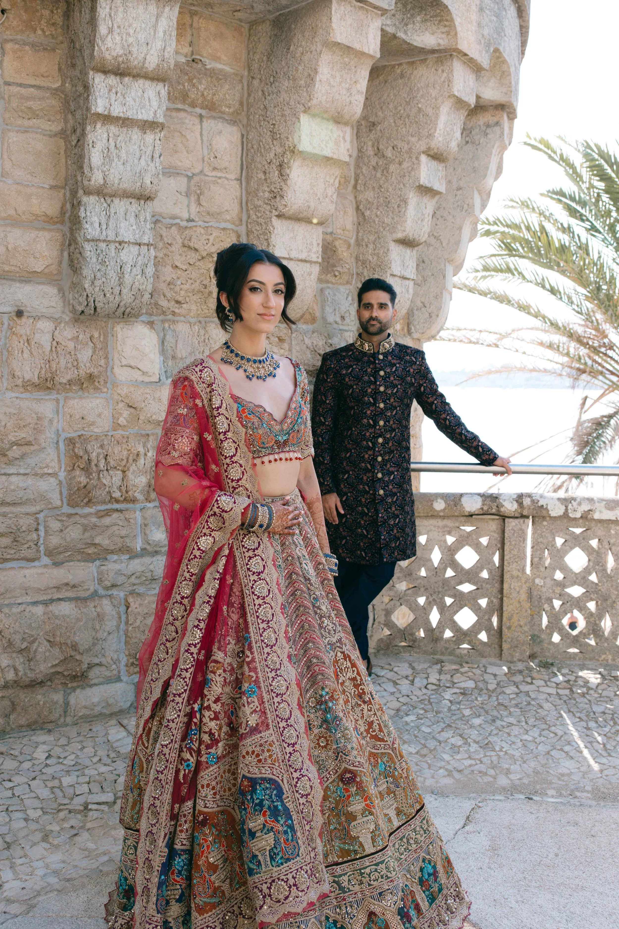 Bride in a red embroidered dress and groom in a dark suit at a coastal stone venue in Marbella