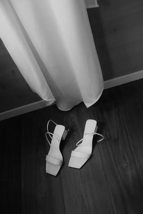 White hanging silk wedding dress with designer heels on a wooden floor