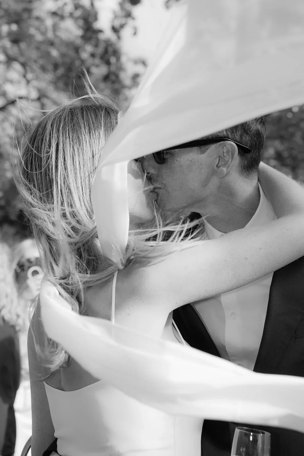 Bride and groom sharing a spontaneous kiss as the veil blows across their faces