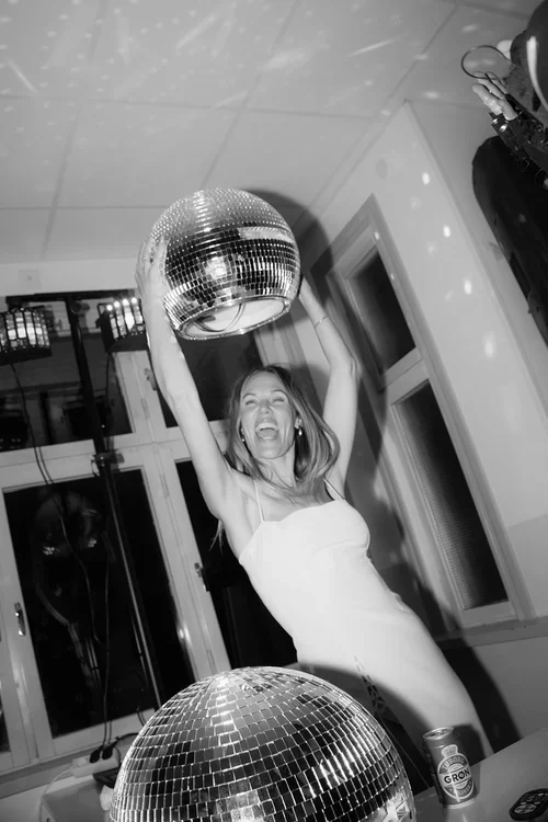 Bride in white dress holding a large mirror disco ball above her head laughing at a Malaga wedding party