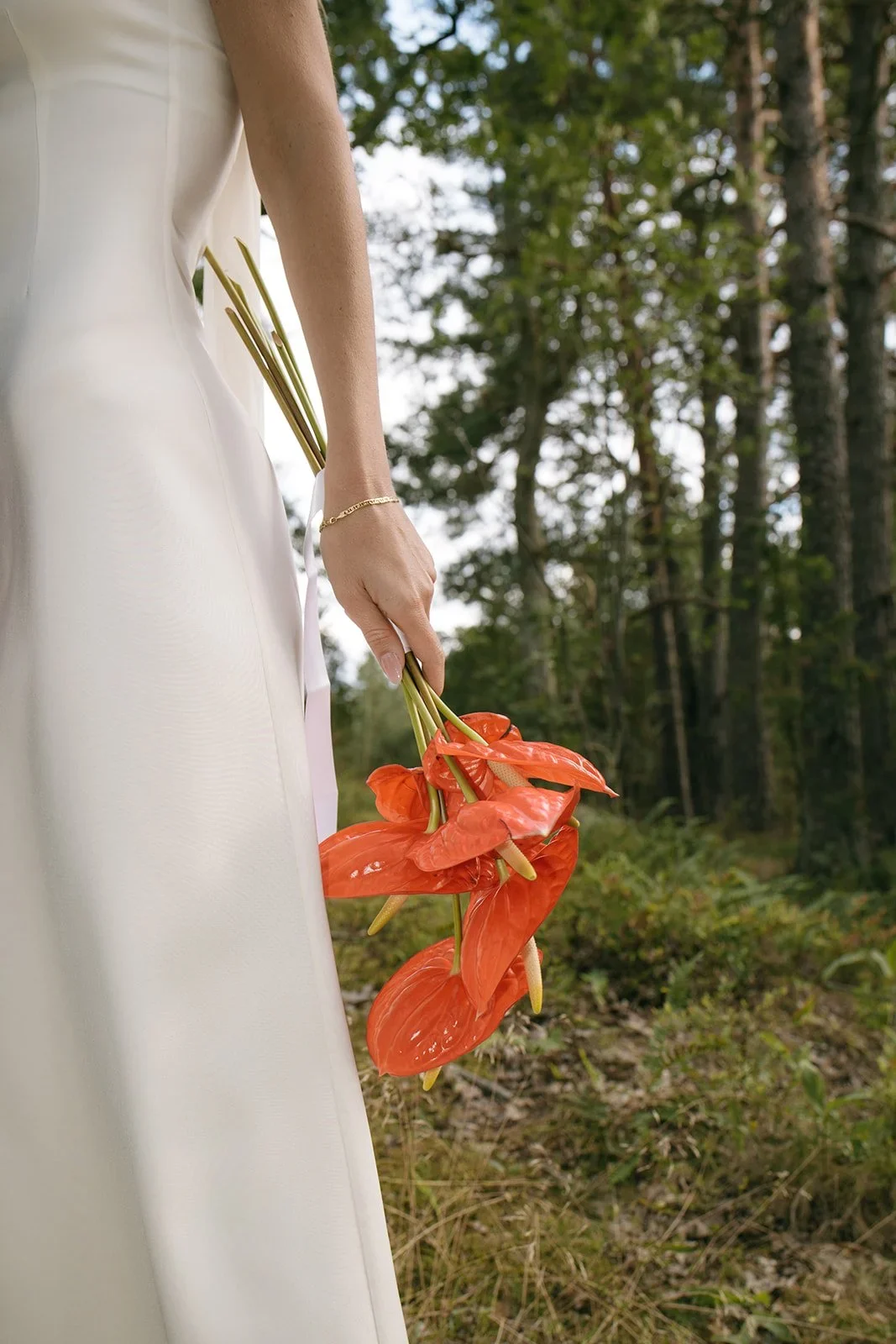 Close-up of bride holding red anthurium flowers in a white wedding dress with a gold bracelet
