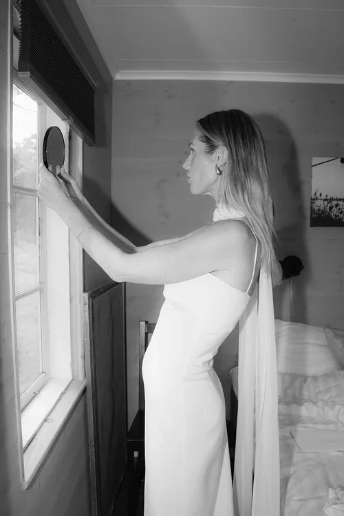 Bride in silk halterneck wedding dress holding a mirror and looking at her reflection in a Marbella hotel room