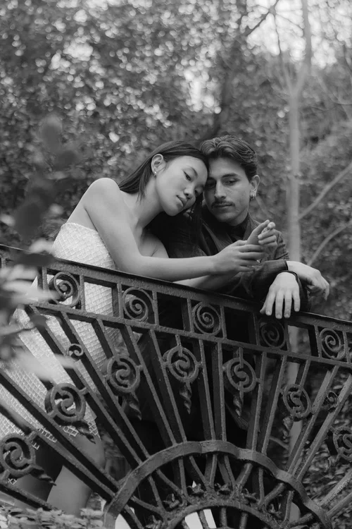 Intimate couple portrait leaning over an ornate wrought iron railing surrounded by lush greenery