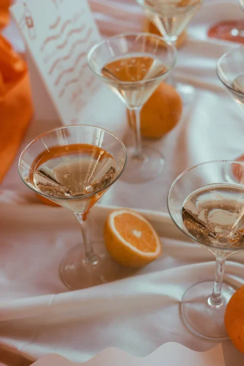 Espresso martini cocktails in coupe glasses alongside halved oranges on an orange silk draped Marbella wedding reception table, styled drinks photography Costa del Sol