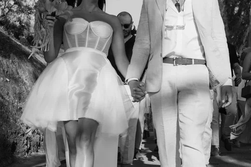 Bride wearing a cropped wedding dress and groom in beige linen suit holding hands after their wedding ceremony