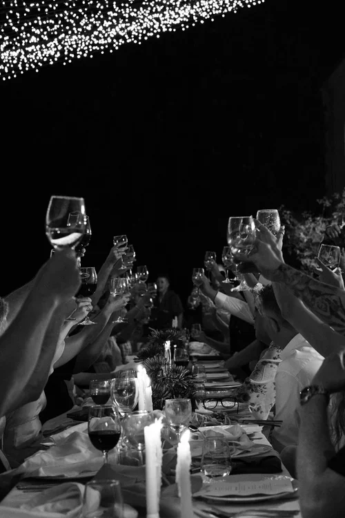 Wedding guests raising wine glasses in a toast along a candlelit reception table under fairy lights at night in Marbella