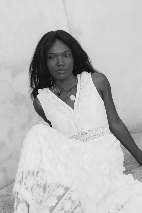  Bride in white sleeveless lace dress sitting against a textured white stone wall
