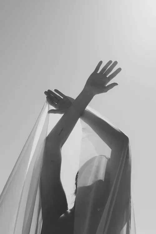 Artistic bridal portrait with flowing white fabric lifted above her hands towards an open sky