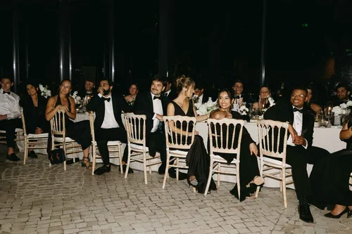 Elegant wedding guests in black tie and formal black dresses seated and chatting at a Malaga wedding reception dinner on a cobblestone outdoor terrace at night