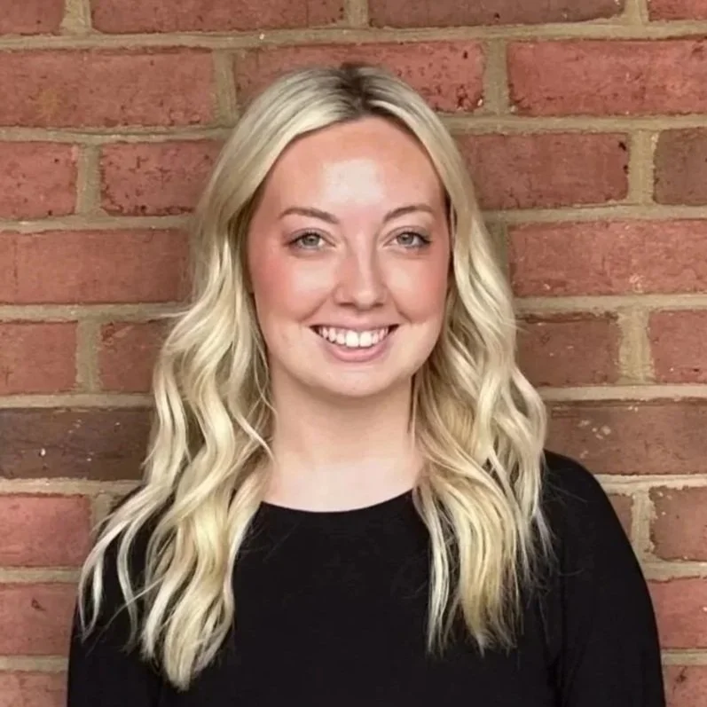 Smiling woman standing in front of a brick wall wearing a black shirt.