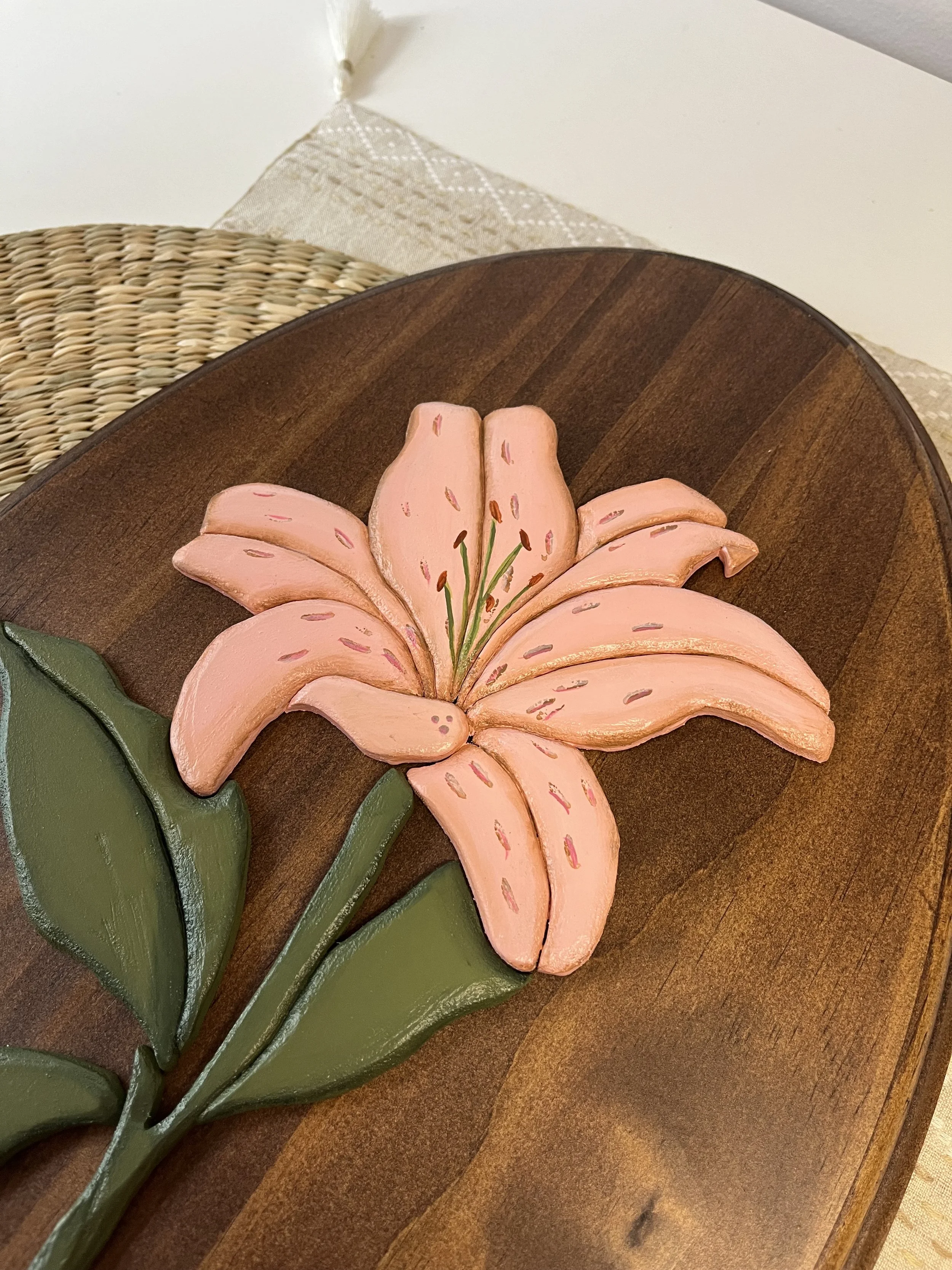 Decorative pink lily flower with green leaves on a dark wooden tray.