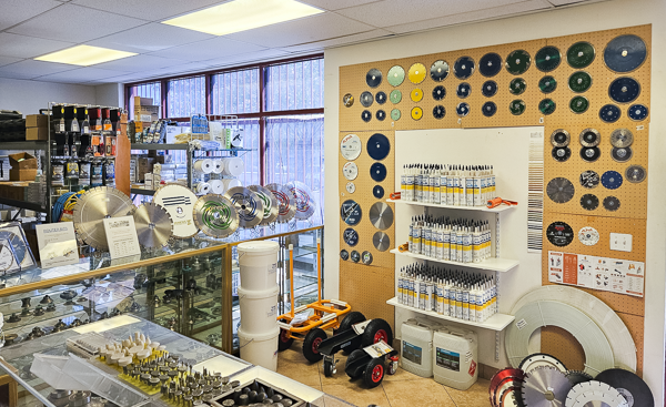 Display of saw blades, cutting tools, and industrial equipment in a hardware store or workshop, with various tool parts on the wall and shelves.