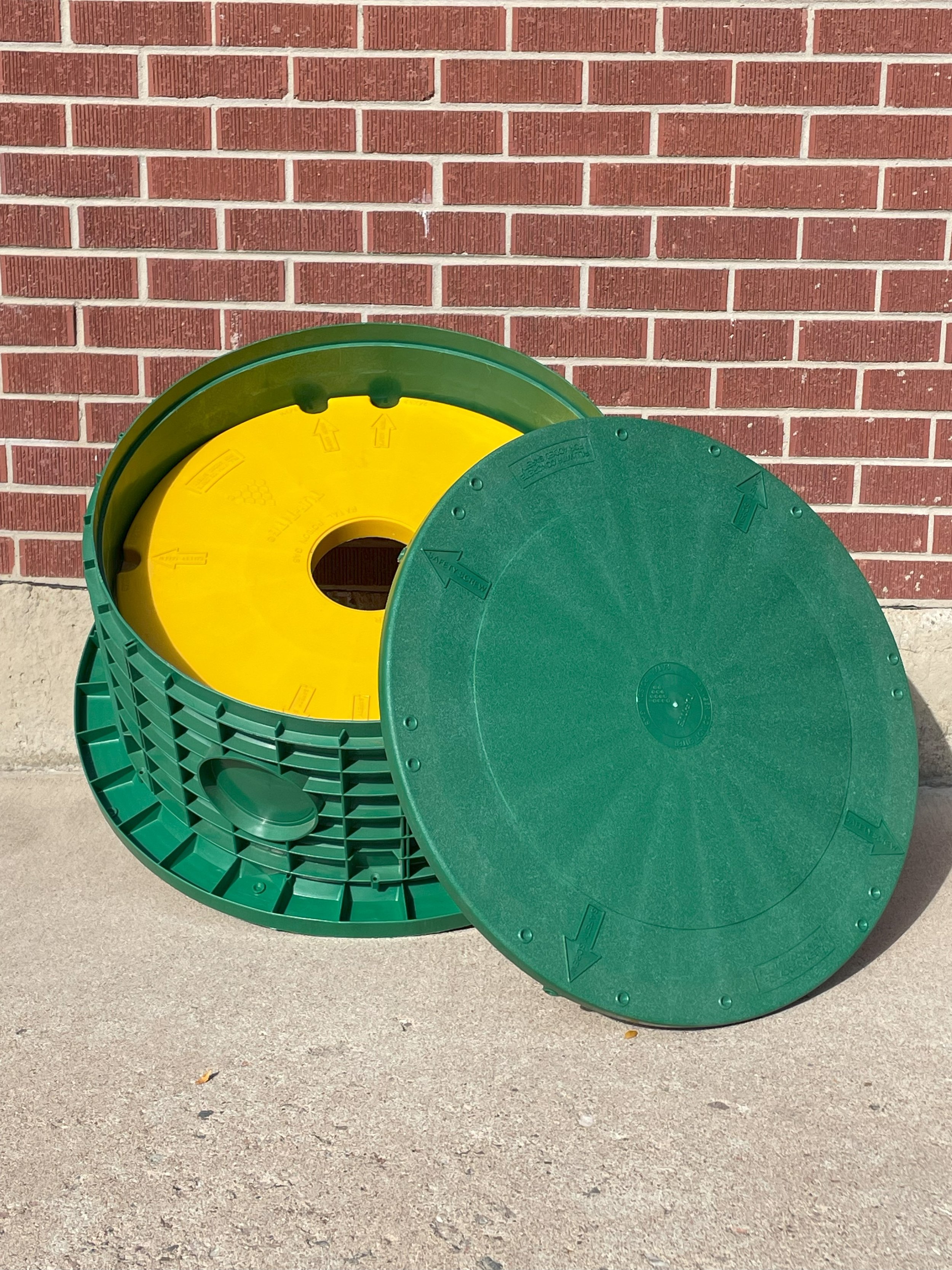 Tuf Tite Brand Septic Risers leaning against a brick wall to display lid, secondary safety lid, and adaptor ring
