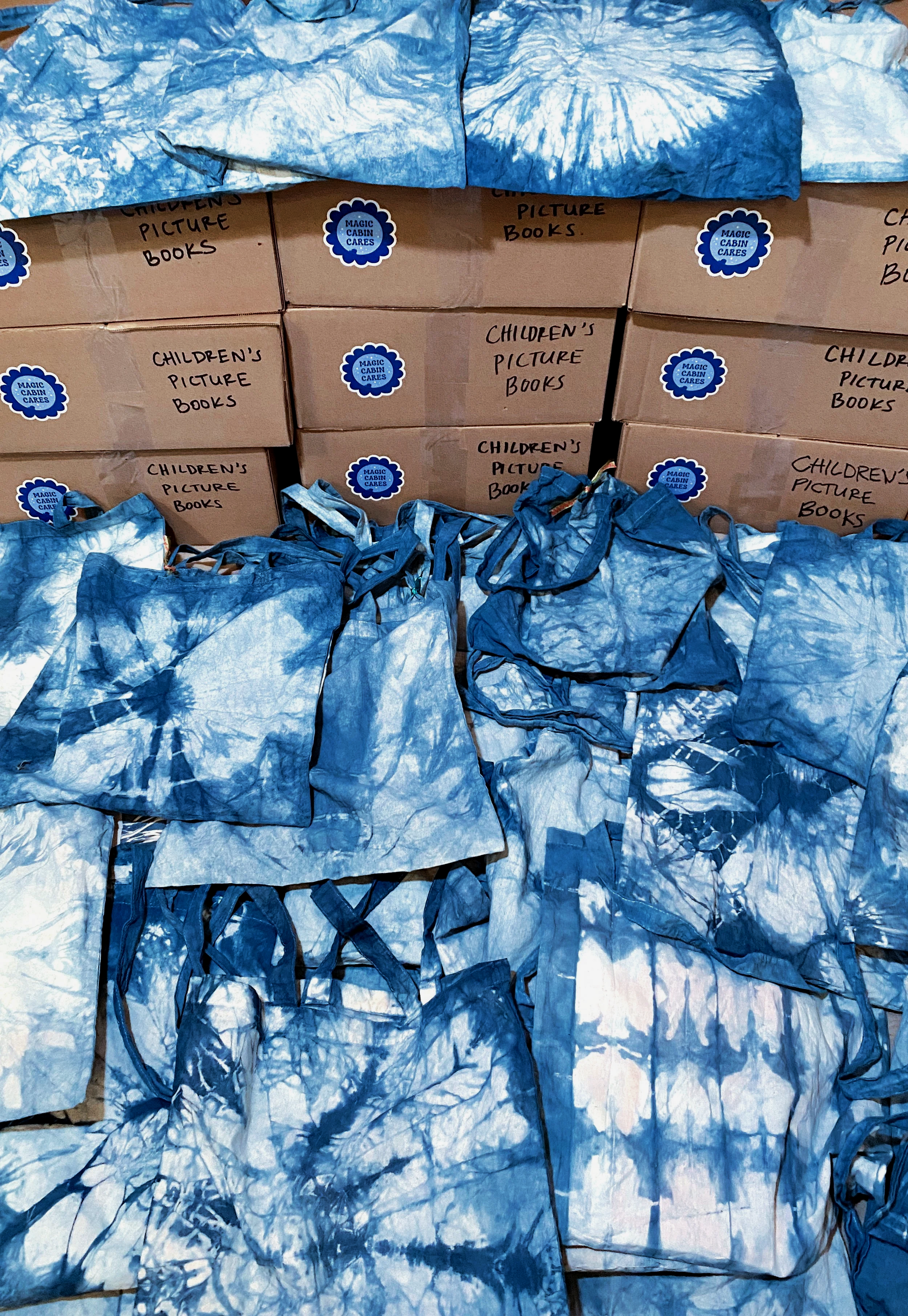Stacks of boxes labeled 'Children's Picture Books' with blue and white tie-dyed drawstring bags in front.