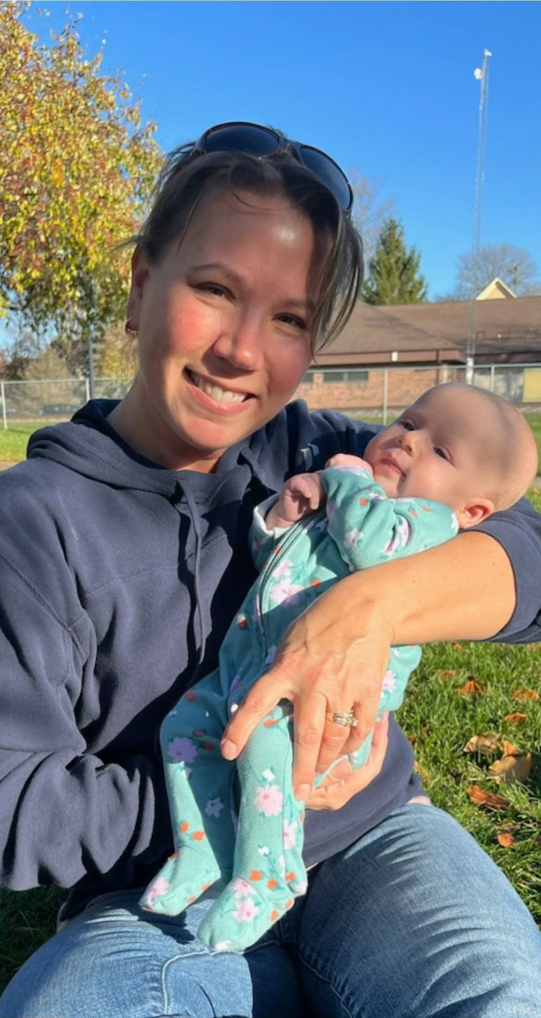 A birth doula holding infant and smiling outside at a park