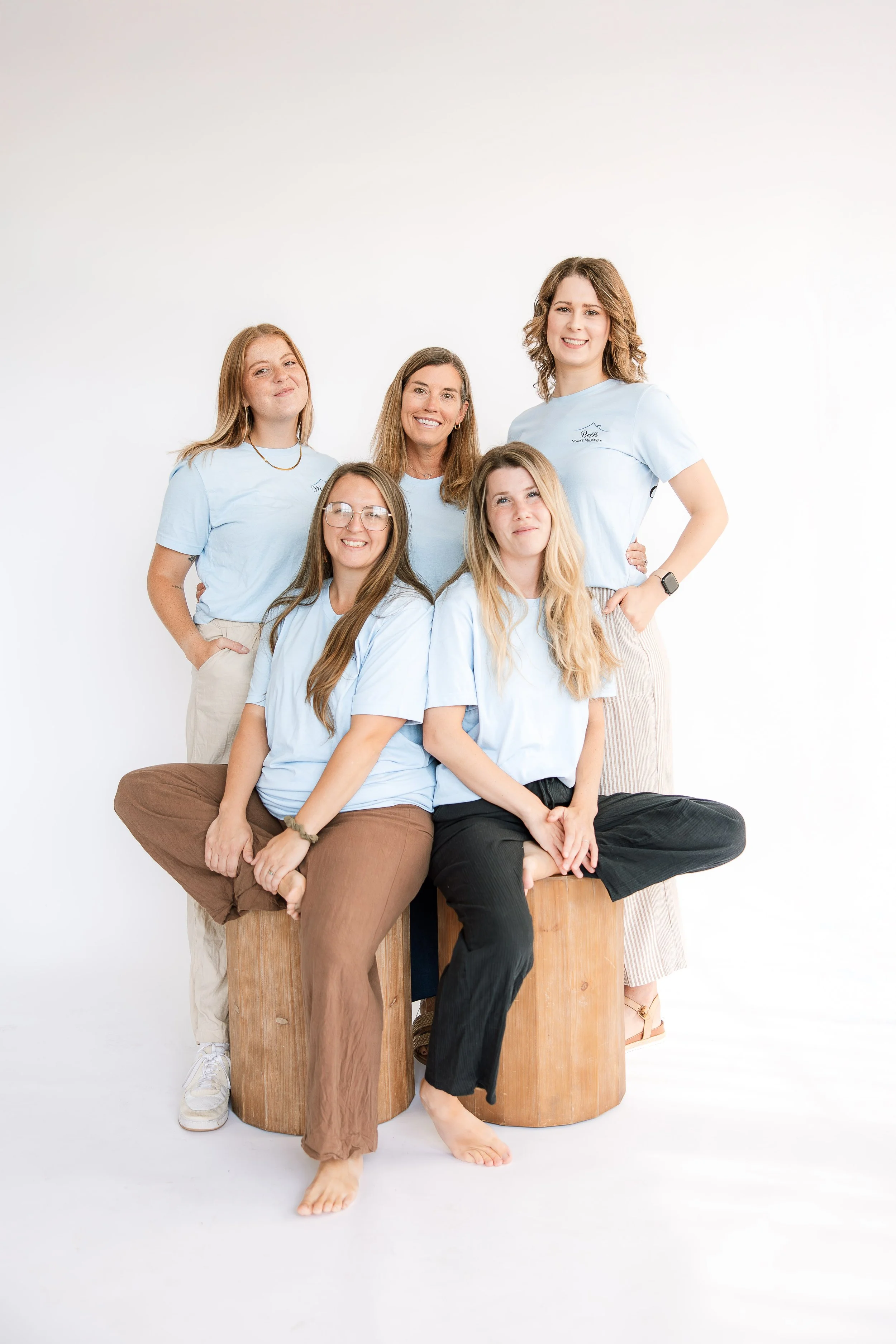 Group of birth doulas in Milwaukee smiling in a group photo with light blue Family Focused Midwifery t-shirts.