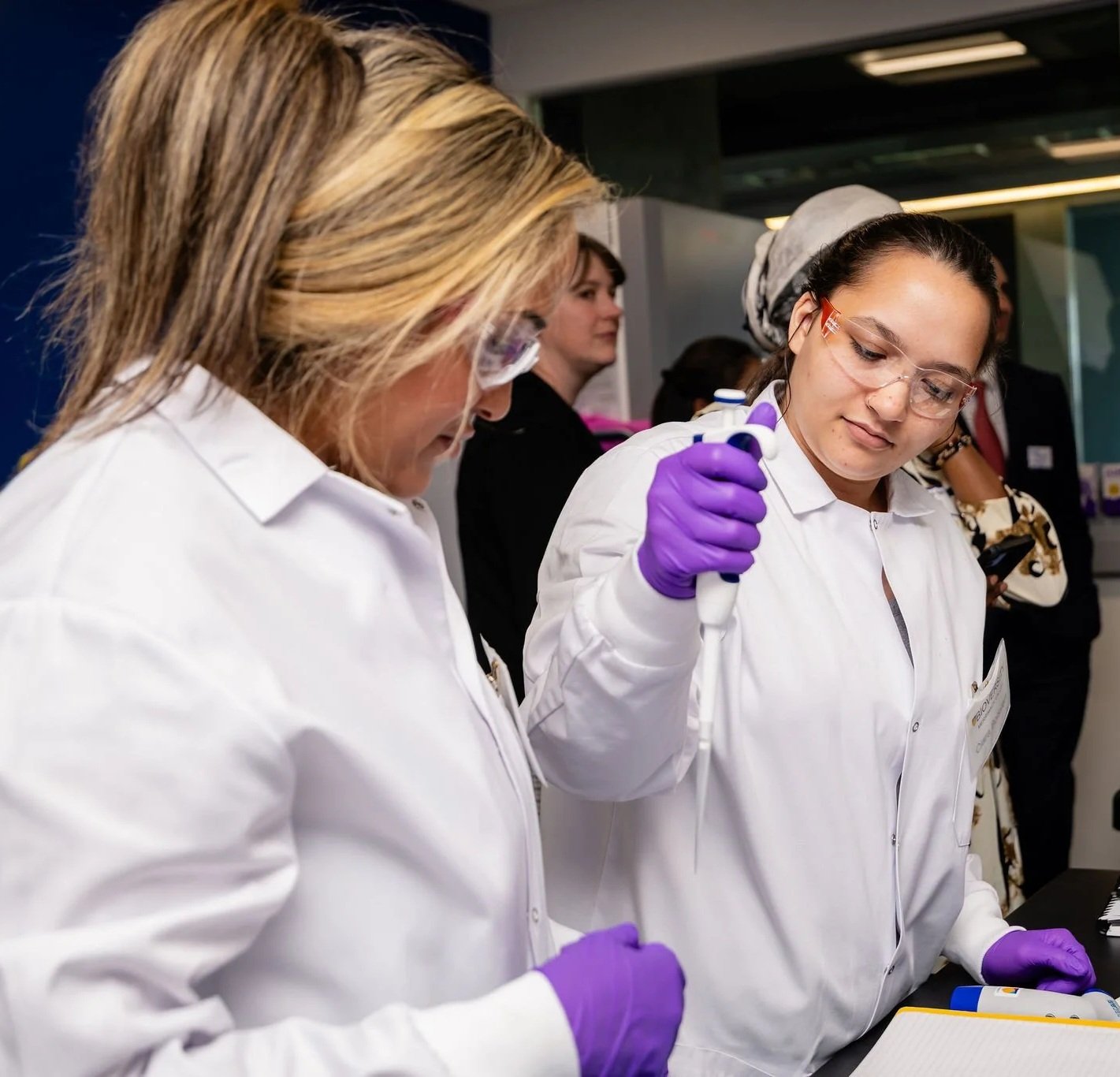 A person uses a pipette while another person looks on.