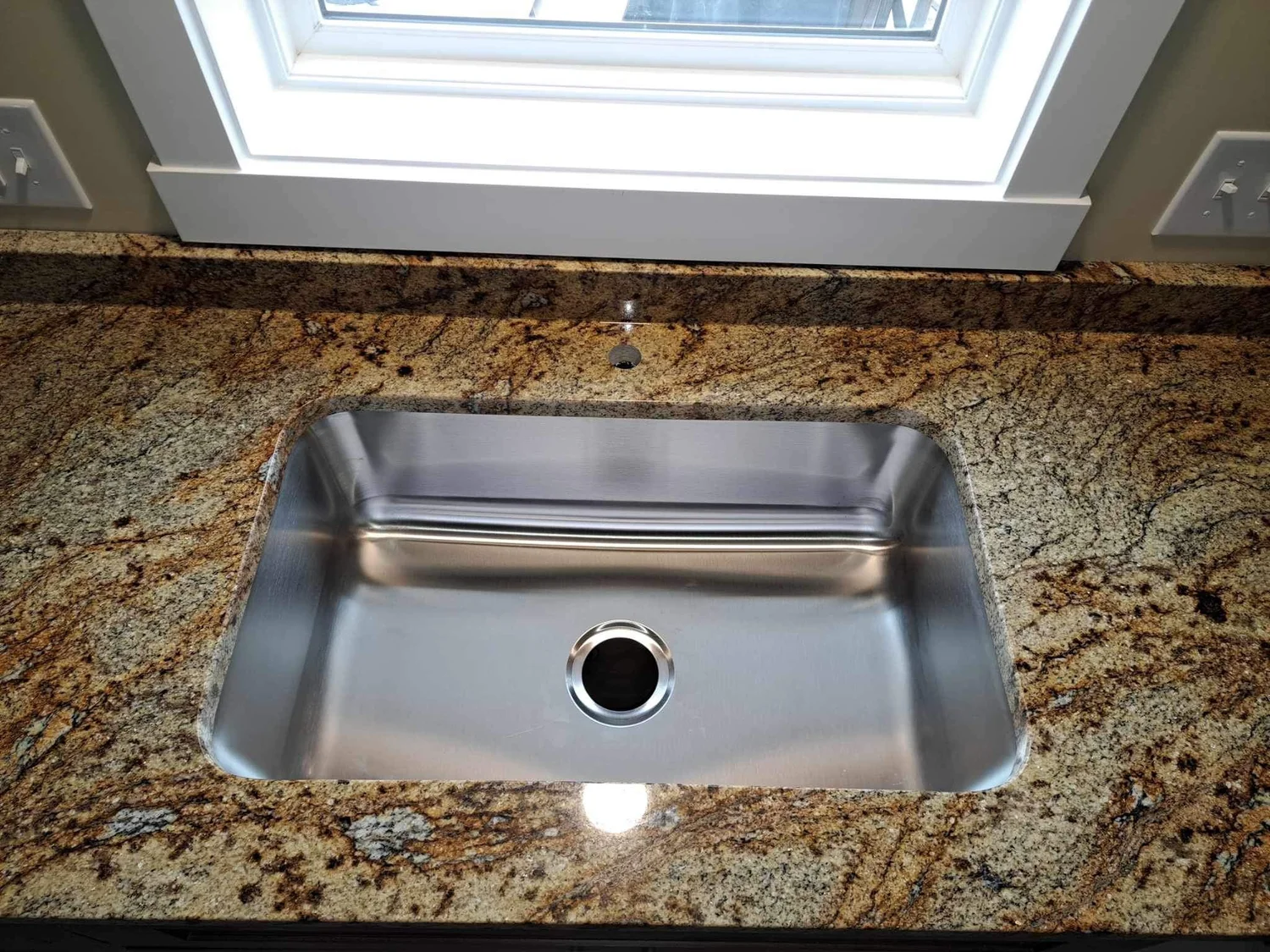 Close-up of a stainless sink cutout in granite with polished edges