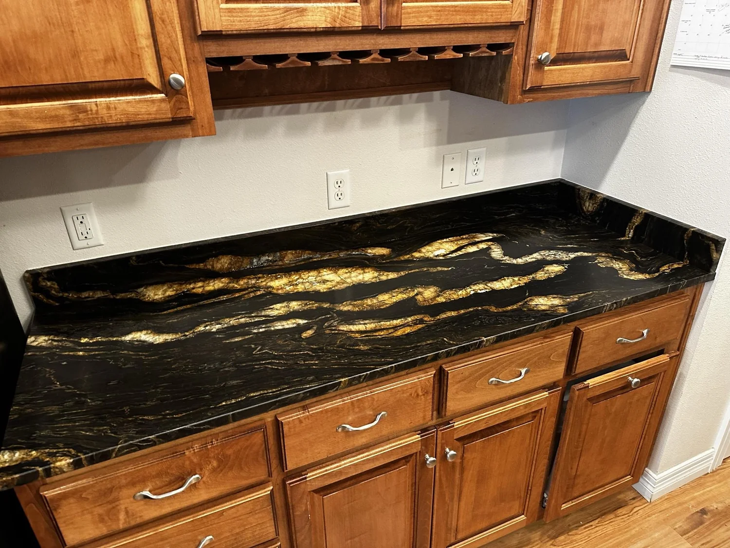 Black granite countertops with gold movement installed along oak cabinetry