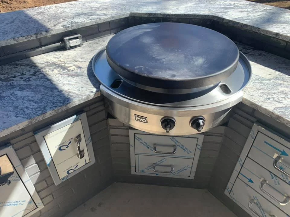Curved stone outdoor counter built around a large round grill