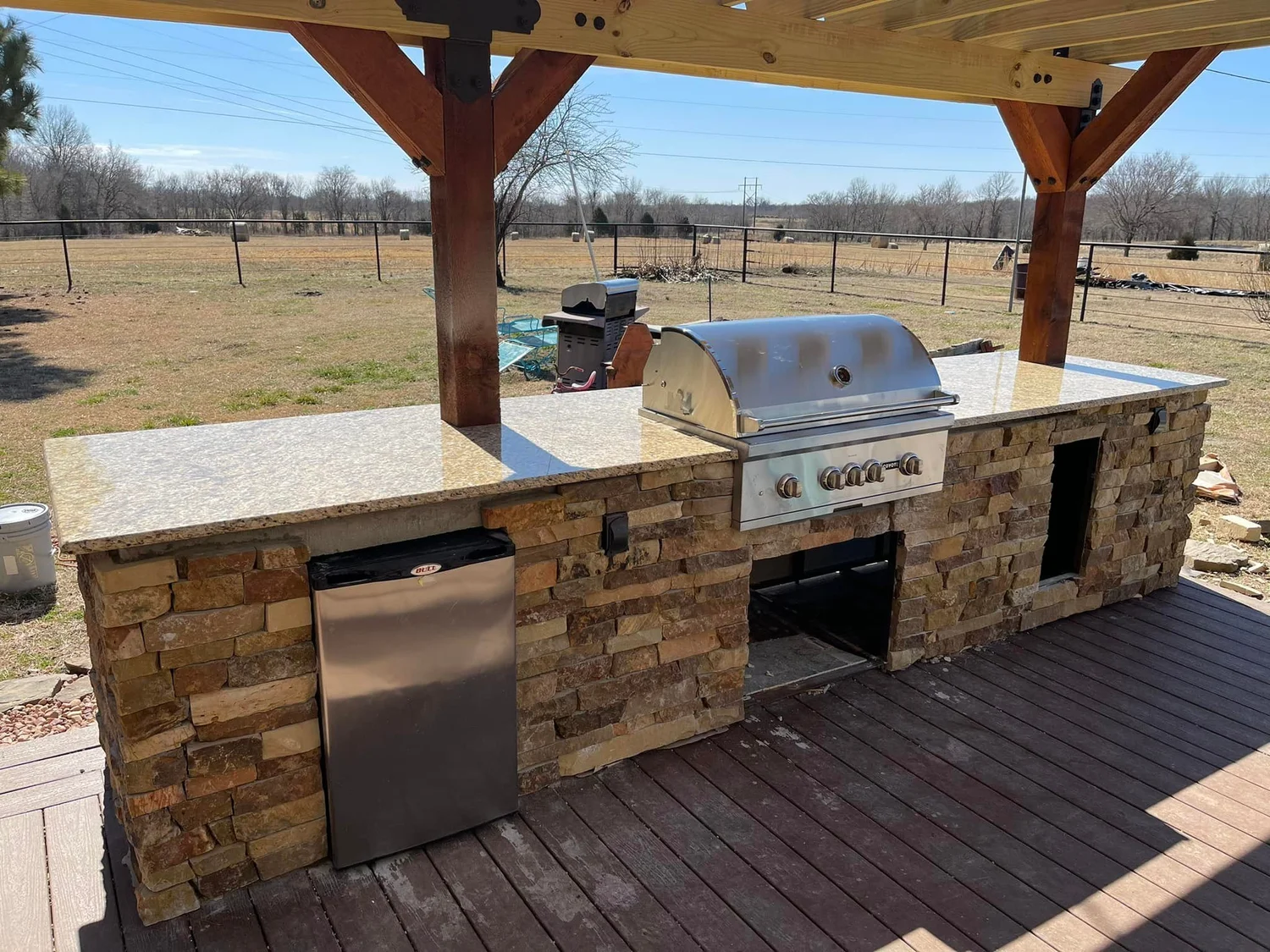 Stone-clad outdoor kitchen with granite top under a cedar pergola