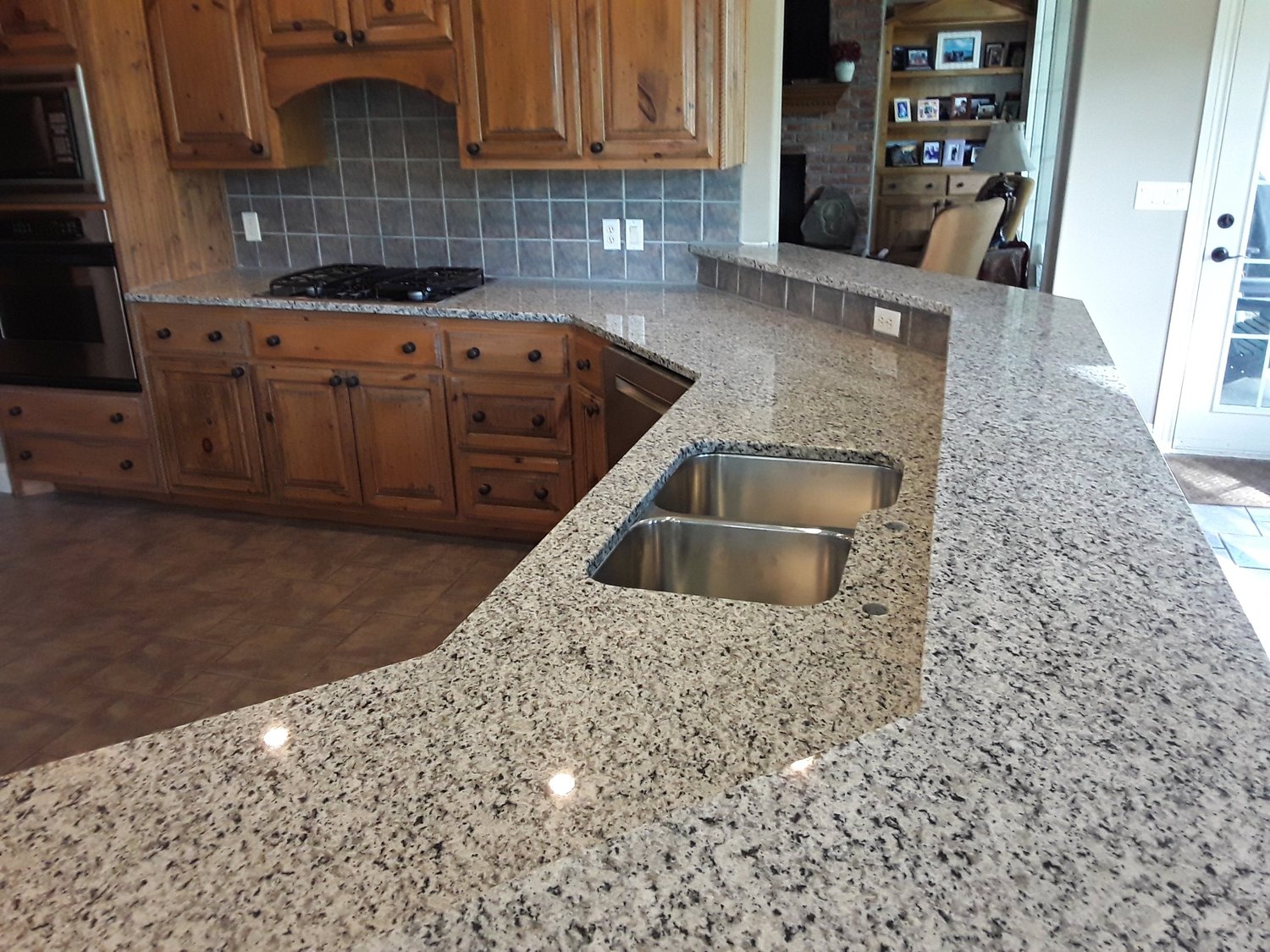 Light granite island with a double-bowl undermount sink and tile backsplash