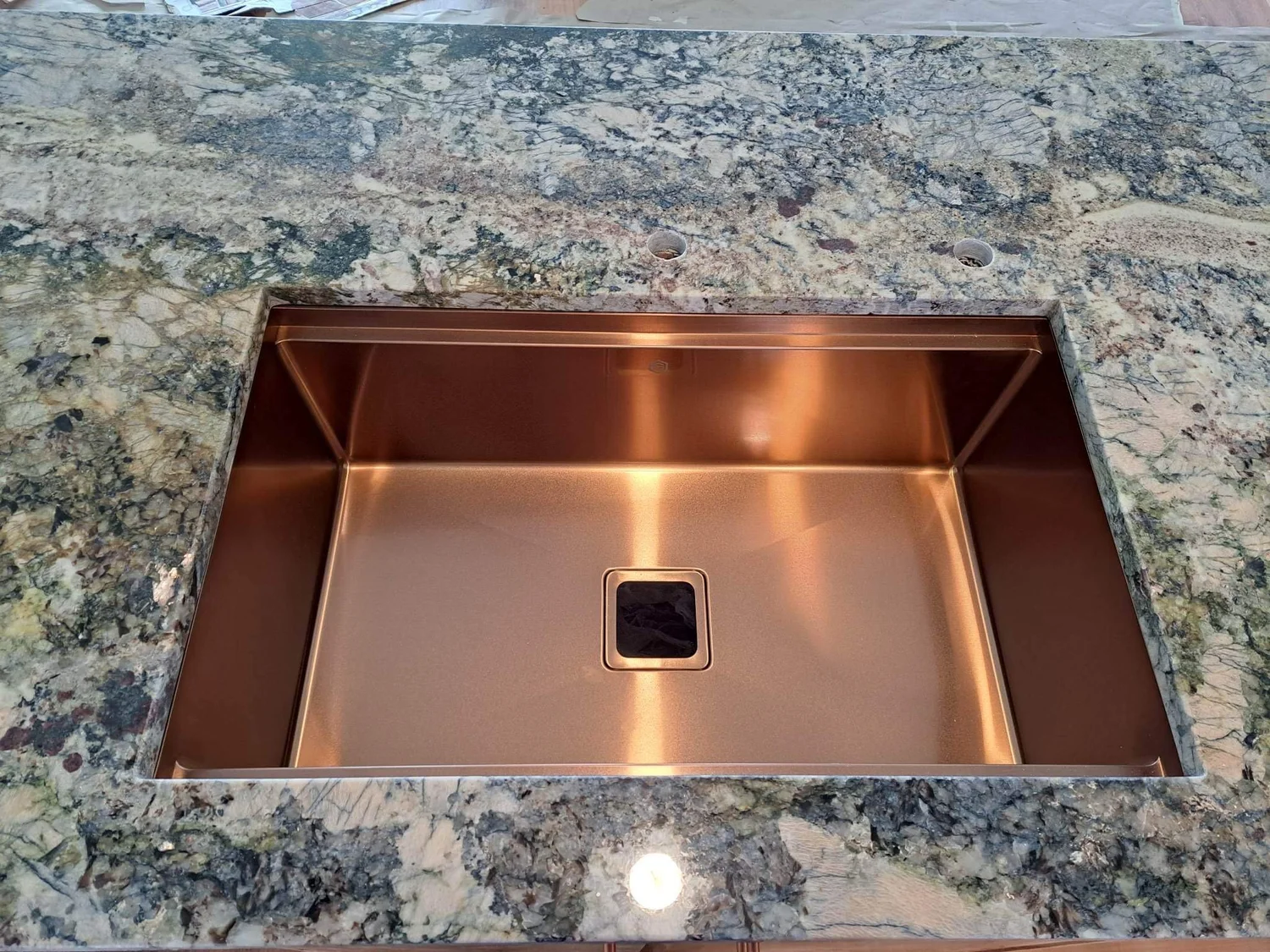 Copper workstation sink installed in a polished granite countertop