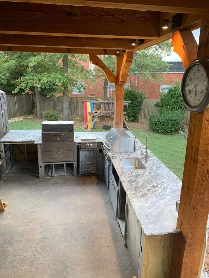 Granite outdoor kitchen countertop under a timber pavilion with dining seating