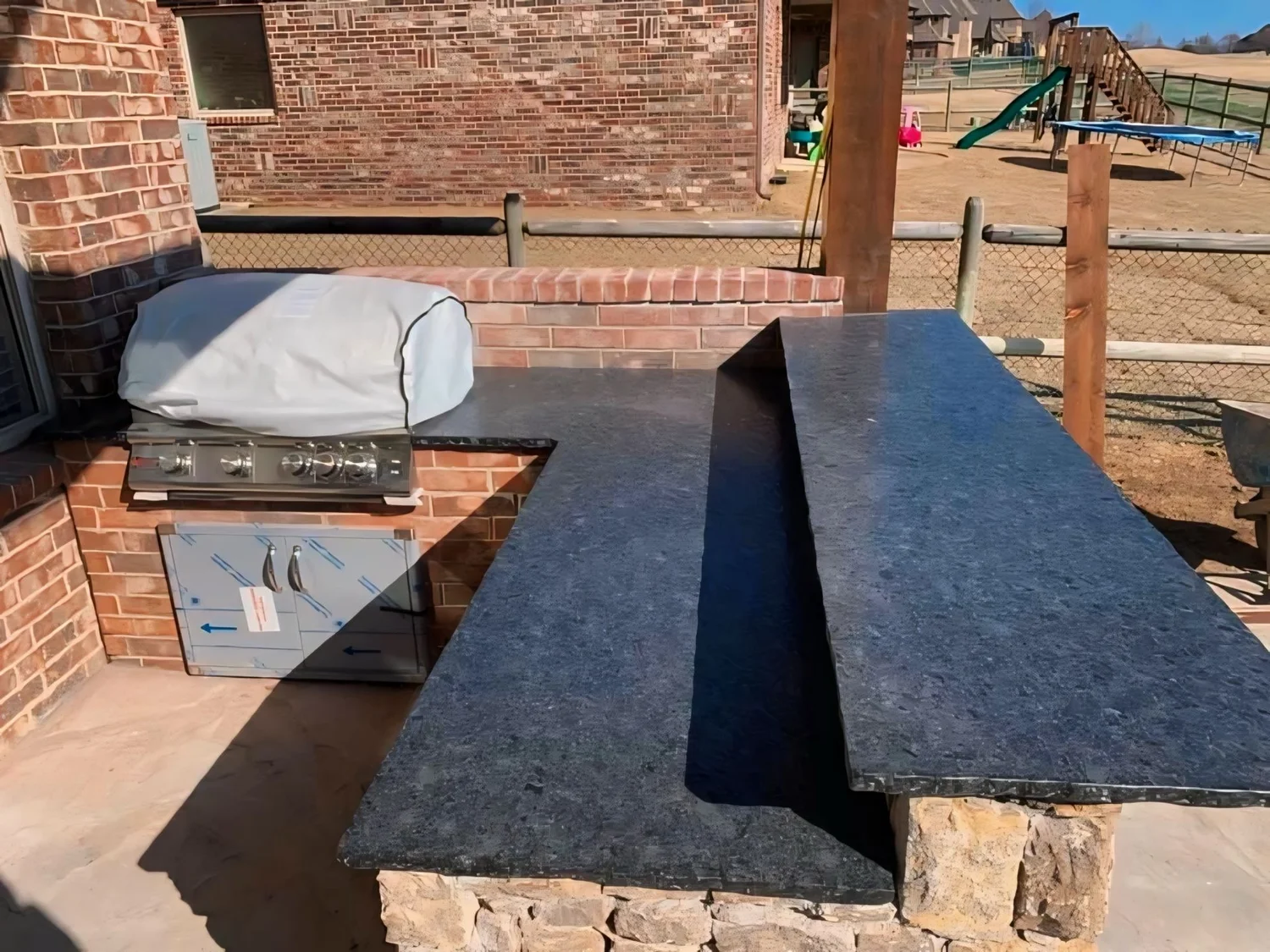 Brick outdoor kitchen with a dark stone countertop and built-in grill