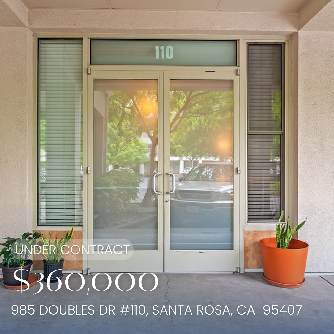 Office building entrance with glass double doors, number 110, and potted plants on either side, reflected trees and cars outside.