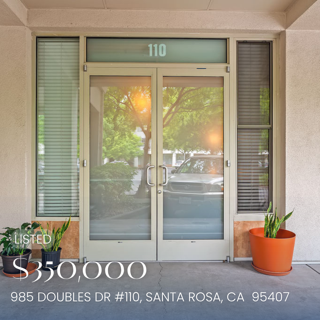 Office building entrance with glass double doors, number 110, and potted plants on either side, reflected trees and cars outside.