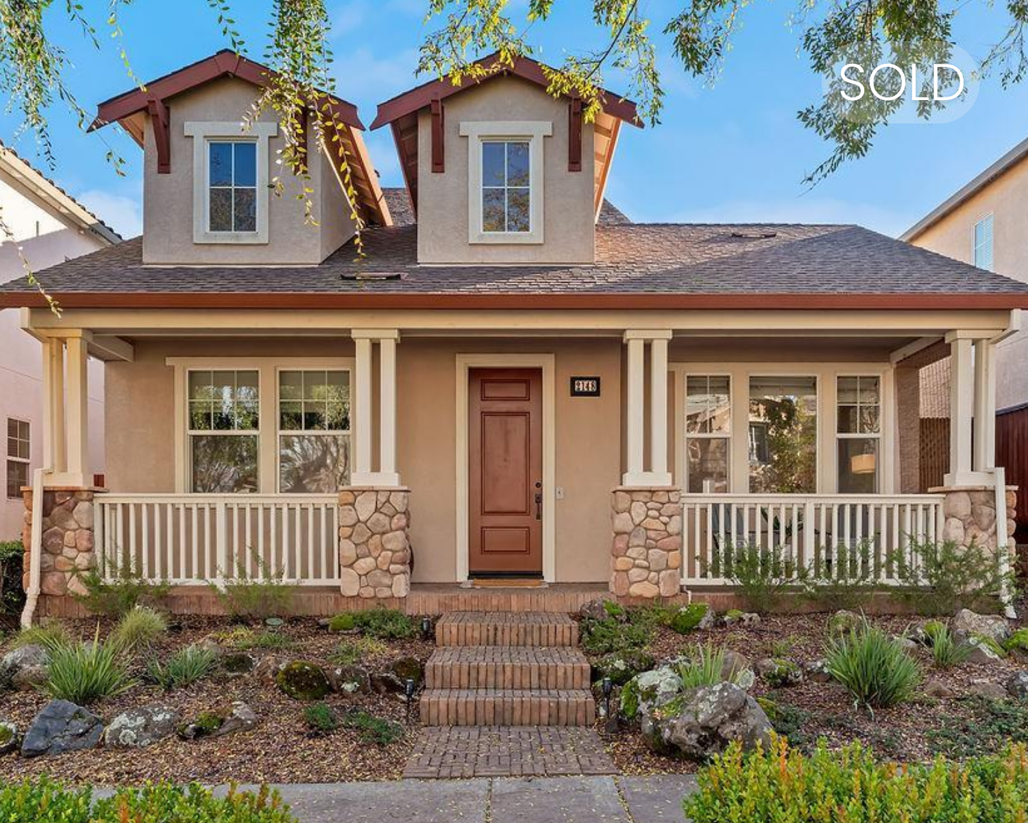Front view of a house with a porch, stone pillars, and a brown wooden door, with a