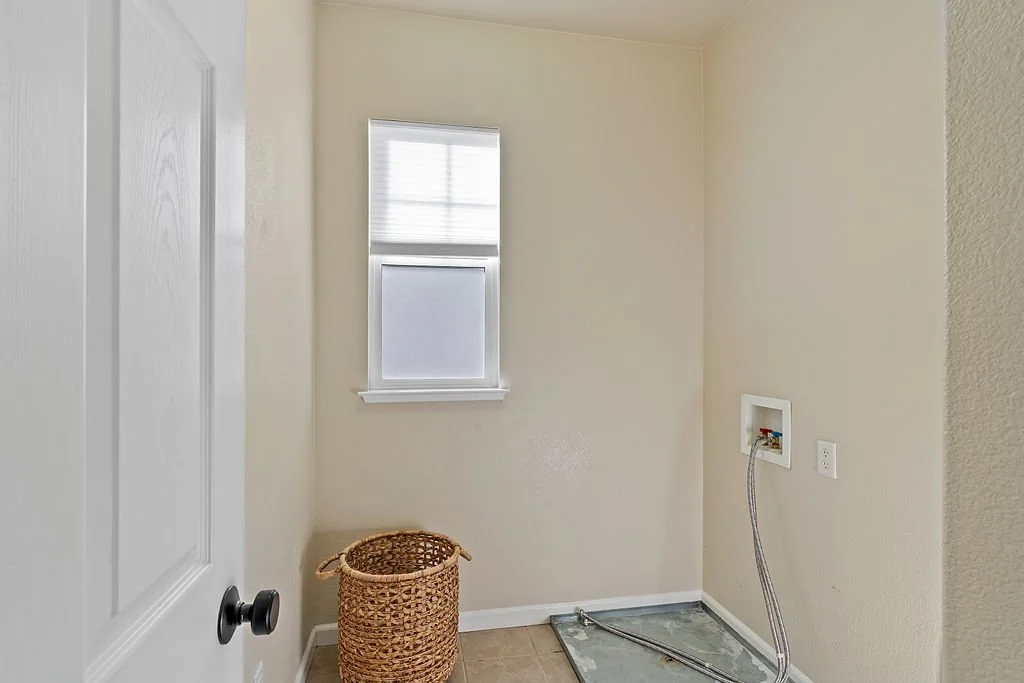 Empty laundry room with a small window, a woven basket, and plumbing connections for a washer on the wall.