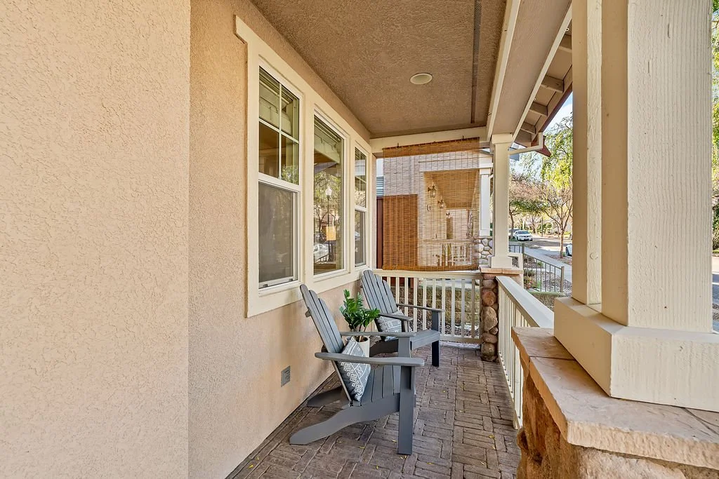 A porch with two grey Adirondack chairs, a potted plant, and a view of the street with trees and cars.