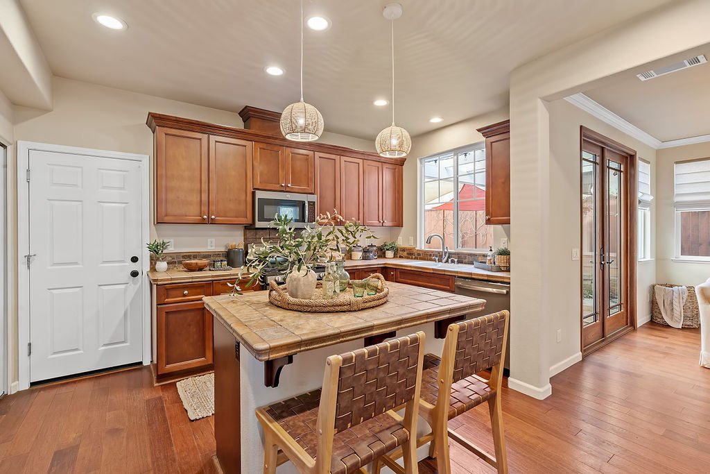 Kitchen with wooden cabinets, a small dining table with two chairs, a window, sliding glass door, and pendant lights.