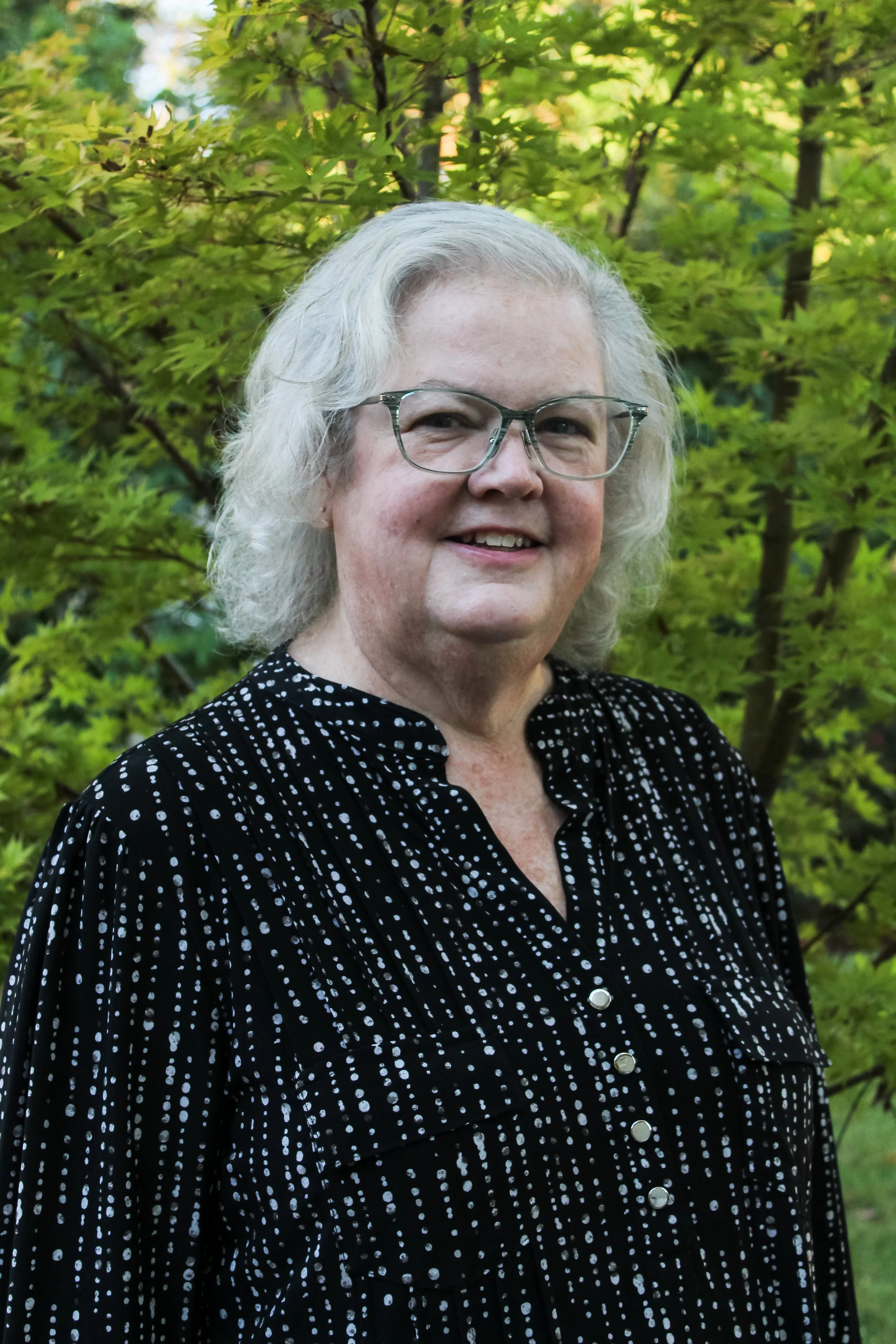 A woman with silver-gray hair, black-rimmed glasses and black cardigan.