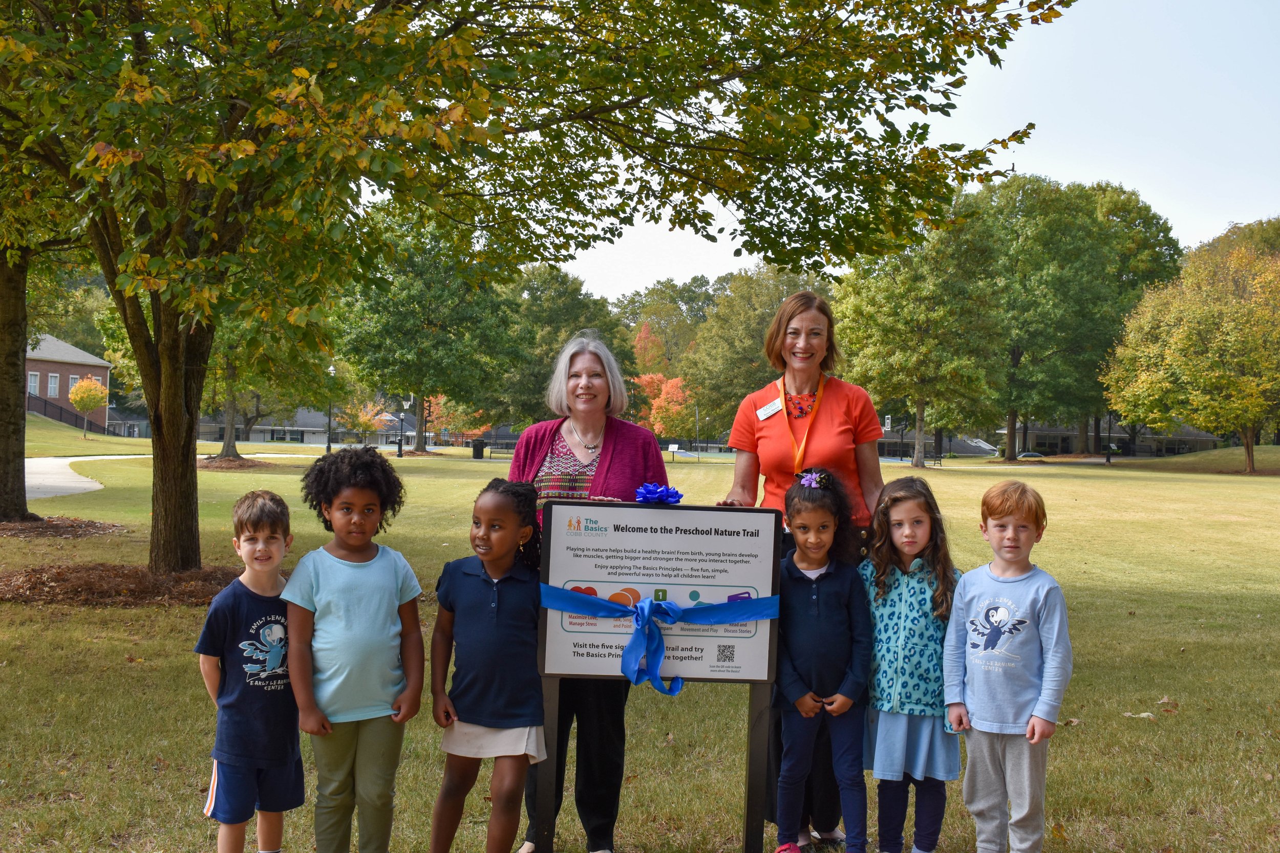Six children and two adults stand smiling around a nature trail sign with a bow.
